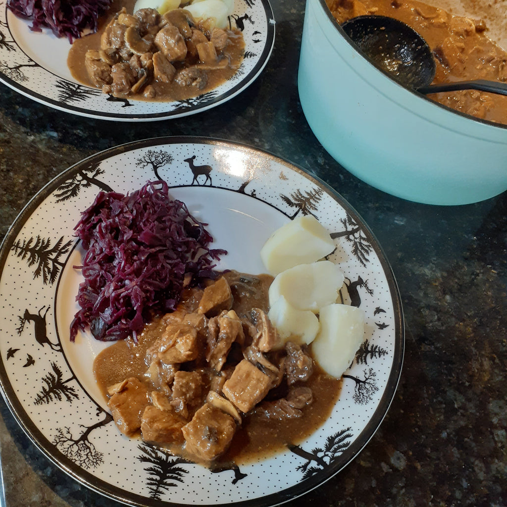 A plate with goulash, red cabbage and potatoes
